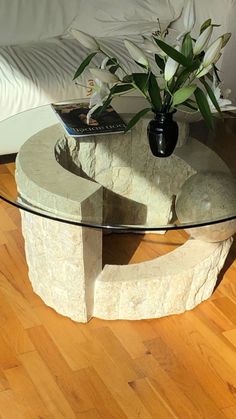 a glass table with flowers on it in front of a white couch and wooden floor