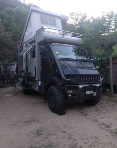 a black truck with a camper attached to it's side in front of some trees