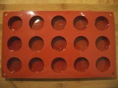 an orange muffin tray sitting on top of a wooden table with lots of holes in it