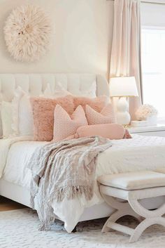 a white bed with pink pillows and blankets on it's headboard in a bedroom