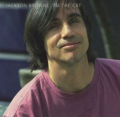 a man with long hair wearing a pink t - shirt and looking off to the side