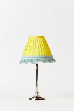 a yellow lamp with a blue shade on it's base and a white wall in the background