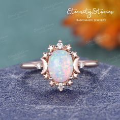 an opal and diamond ring sits on top of a blue rock with flowers in the background