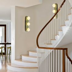 a white staircase with some lights on the wall and chairs in the room next to it