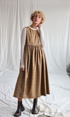 a woman standing in front of a white backdrop wearing a brown dress and black boots