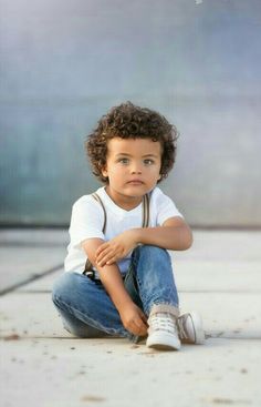 a little boy sitting on the ground with his legs crossed and looking at the camera