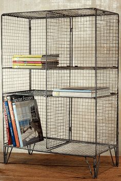 a metal shelf with books and magazines in it on top of a wooden floor next to a wall