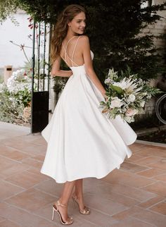 a woman in a white dress holding a bouquet and wearing high heeled sandals with her hand on her hip