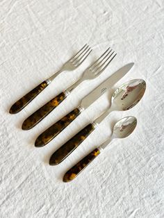 four forks, two spoons and one knife on a white tablecloth with brown spots