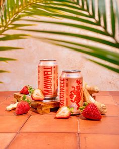 some strawberries and bananas are sitting on the ground next to two cans of strawberry soda