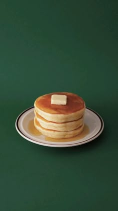 a stack of pancakes with butter on top sitting on a white plate against a green background