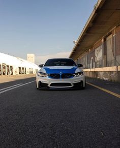 a white and blue car is parked on the street next to a large building with an overpass