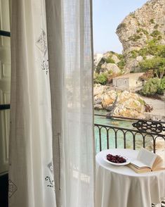 an open book sitting on top of a table next to a window with sheer curtains