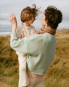 a woman holding a child in her arms while standing on top of a grass covered field