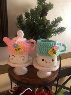 two crocheted cups sitting on top of a table next to a potted plant