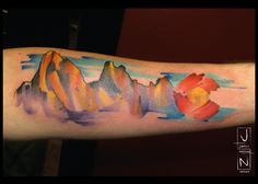 a watercolor painting style arm tattoo with mountains and flowers on the left inner arm