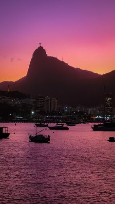 boats are floating in the water at sunset with a mountain in the backgroud