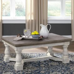 a white coffee table with fruit on it in front of a window and blue rug