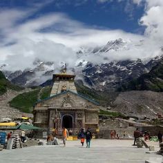 people are walking around in front of a small building with mountains in the background and clouds overhead