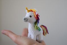 a small crocheted unicorn toy sitting on top of someone's hand in front of a white wall