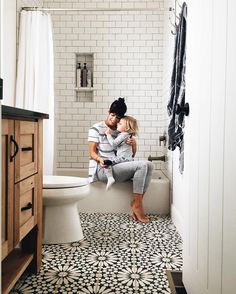 a man and woman sitting on top of a toilet in a bathroom