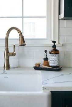 a white sink sitting under a window next to a faucet and soap dispenser