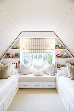 a bedroom with two white beds sitting under a window next to a shelf filled with books