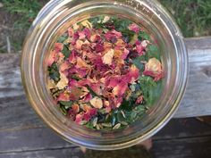 a glass jar filled with dried flowers on top of a wooden table next to grass