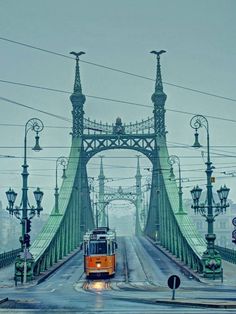 an orange train traveling over a bridge in the foggy day with street lamps on either side