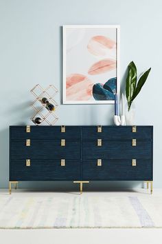 a blue dresser with gold handles and drawers in front of a painting on the wall