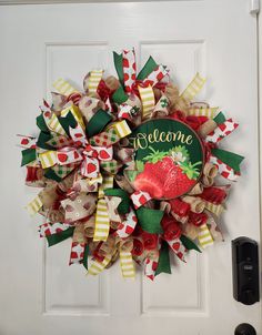 a welcome wreath on the front door with red and green ribbons hanging from it's side