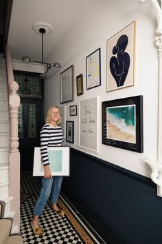 a woman standing in front of a wall with pictures on it and holding a piece of paper