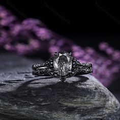 a close up of a ring on a rock with purple flowers in the back ground