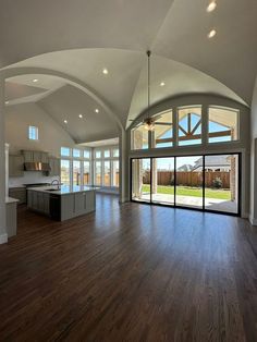 an empty living room with wood flooring and large glass doors leading to the kitchen