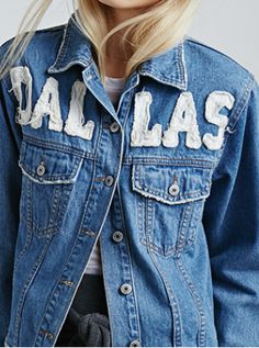 a woman wearing a denim jacket with the word dallas painted on it