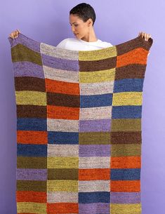 a woman holding up a multicolored blanket in front of her face on a purple background