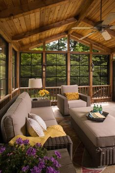 a covered porch with wicker furniture and flowers on the table in front of it