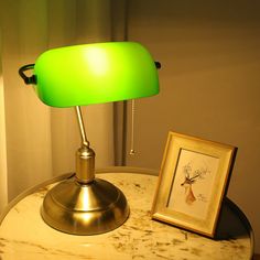 a green lamp sitting on top of a white table next to a framed picture and a painting