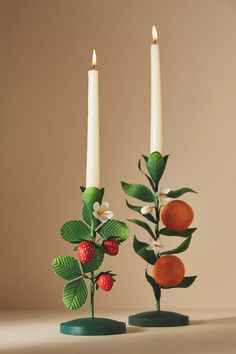 two candles with fruit and leaves on them