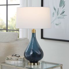 a blue vase sitting on top of a glass table next to a white lamp shade