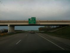 an overpass with two green street signs above it and cars on the road below