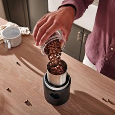 a person pouring coffee into a grinder on top of a wooden table in a kitchen