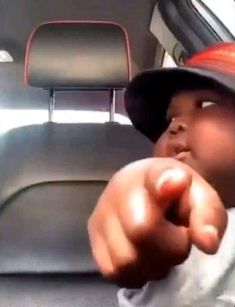 a young boy wearing a hat and pointing at something in the back seat of a car