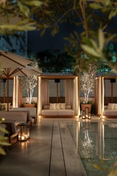 an outdoor lounge area at night with lit up seating and umbrellas over the pool