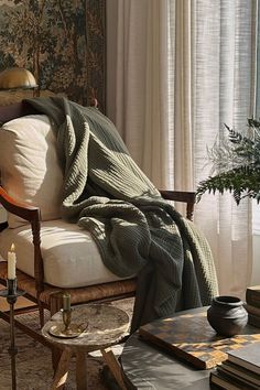 a chair with a blanket on it in front of a window and a coffee table