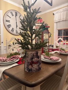 a small christmas tree in a pot on top of a wooden table with plates and utensils