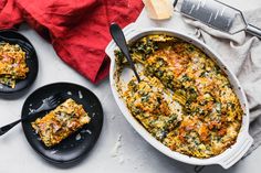 a casserole dish with spinach, cheese and bread in it next to two black plates