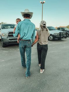 a man and woman walking in a parking lot with cars behind them on a sunny day