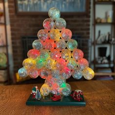 a christmas tree made out of plastic balls on top of a wooden table in front of a fireplace