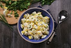 a blue bowl filled with potato salad next to a wooden cutting board and spoons